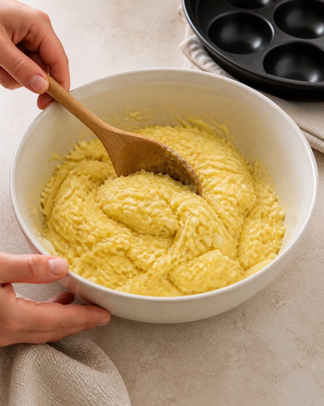One single photorealistic instructional frame of the cohesive patty mixture being folded in one bowl for Rösti - lavet i æbleskivepanden, featuring kartofler, løg, æg, with only the named equipment and no unrelated food, text, logos or packaging under tilberedningen af rösti - lavet i æbleskivepanden