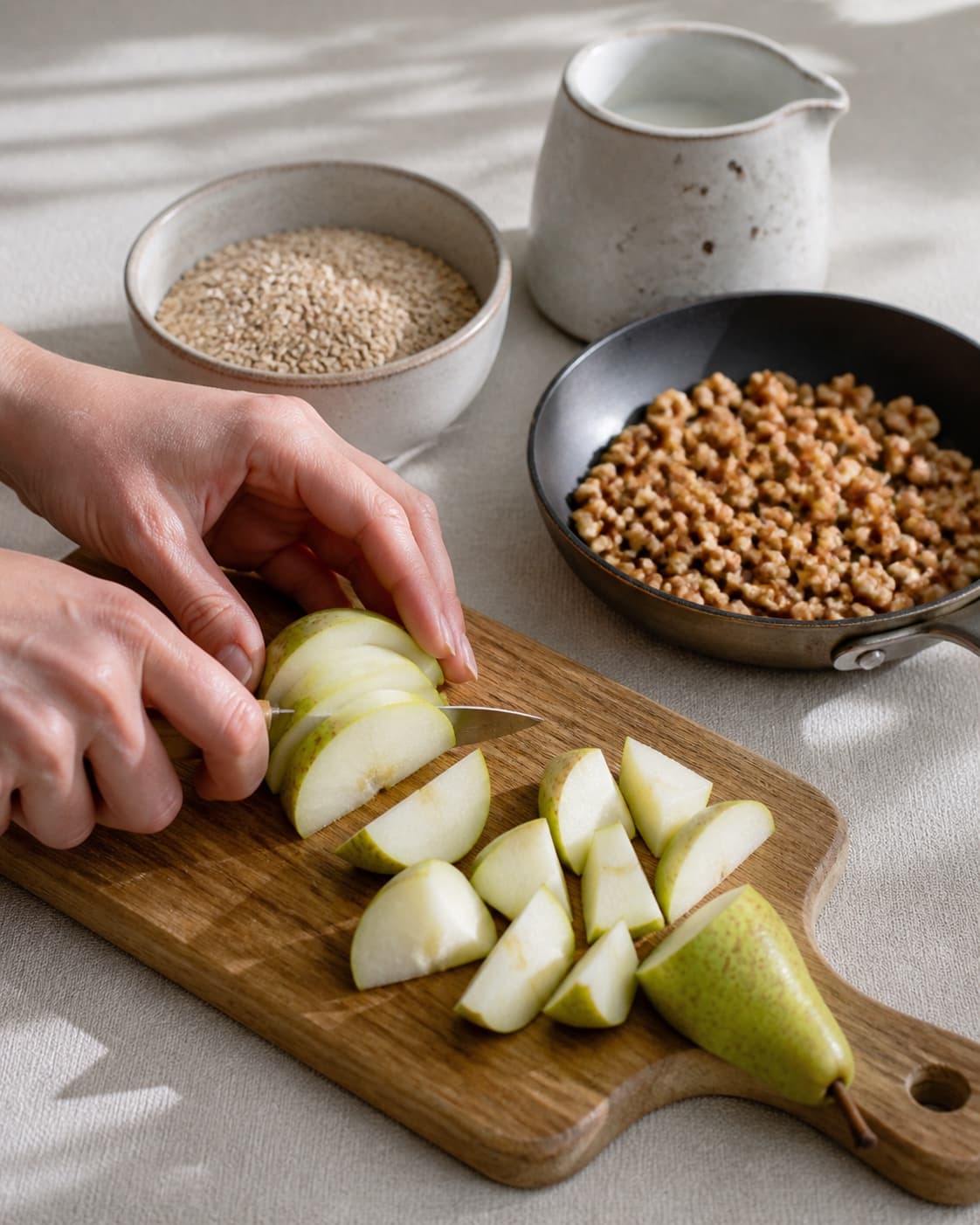 One single photorealistic instructional frame of fresh fruit being cut beside one small pan of toasted topping for Boghvedegrød med pærer og valnødder, featuring boghvedegryn, mælk, pærer, with only the named equipment and no unrelated food, text, logos or packaging under tilberedningen af boghvedegrød med pærer og valnødder