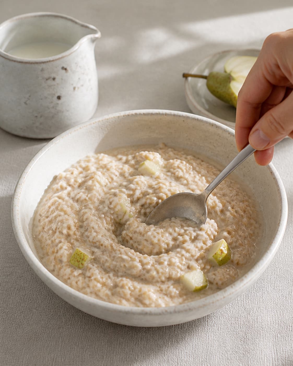 One single photorealistic instructional frame of the porridge consistency being adjusted with a spoon for Boghvedegrød med pærer og valnødder, featuring boghvedegryn, mælk, pærer, with only the named equipment and no unrelated food, text, logos or packaging under tilberedningen af boghvedegrød med pærer og valnødder