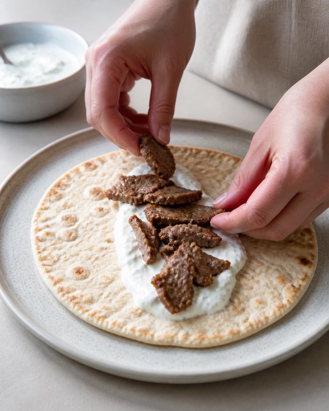 One single photorealistic instructional frame of realistic hands arranging filling down the center of one wrap for Kebab shawarma, featuring lammekød, græsk yoghurt, fladbrød, with only the named equipment and no unrelated food, text, logos or packaging under tilberedningen af kebab shawarma