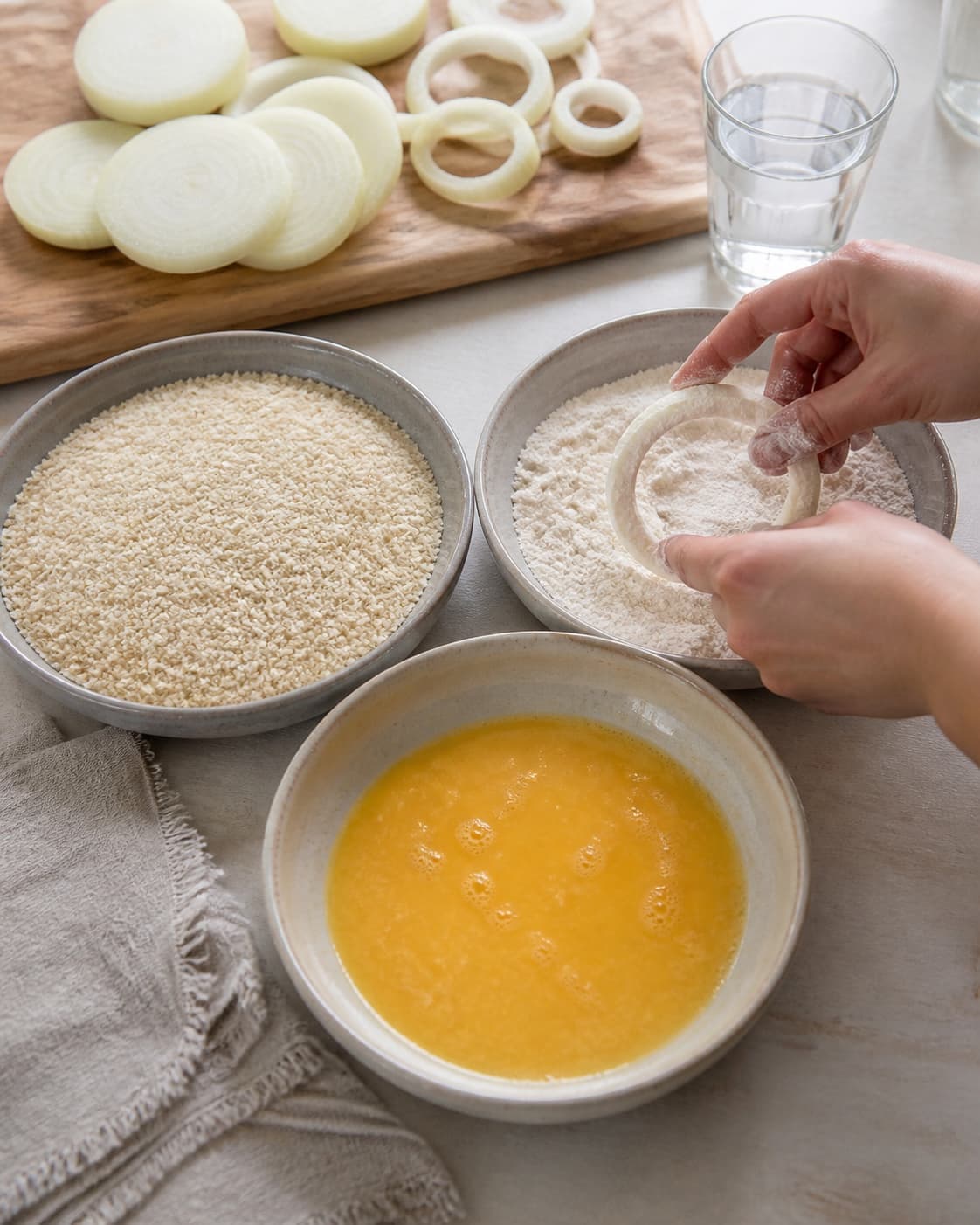 One single photorealistic instructional frame of a clear breading station with flour egg and crumbs for Sprøde løgringe med chilicheese dip, featuring store løg, hvedemel, danskvand, with only the named equipment and no unrelated food, text, logos or packaging under tilberedningen af sprøde løgringe med chilicheese dip