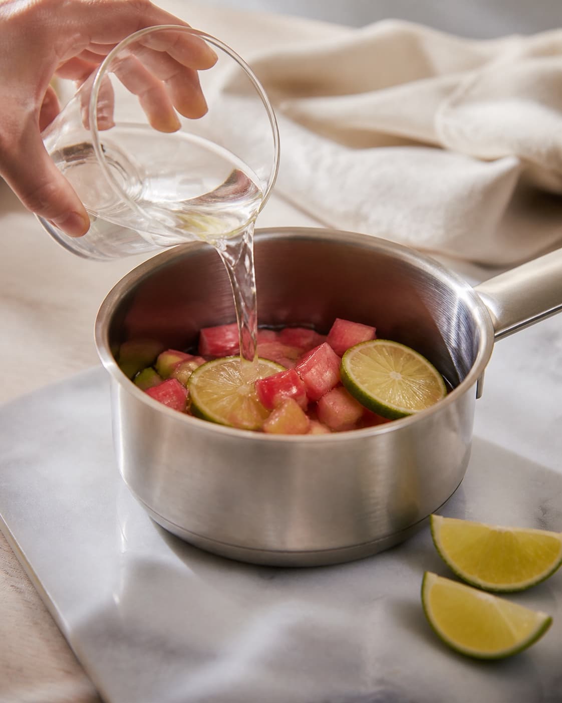 One single photorealistic instructional frame of the aromatic drink base being prepared in one small saucepan for Rabarber Mojito, featuring rabarber, hvid rom, lime, with only the named equipment and no unrelated food, text, logos or packaging under tilberedningen af rabarber mojito