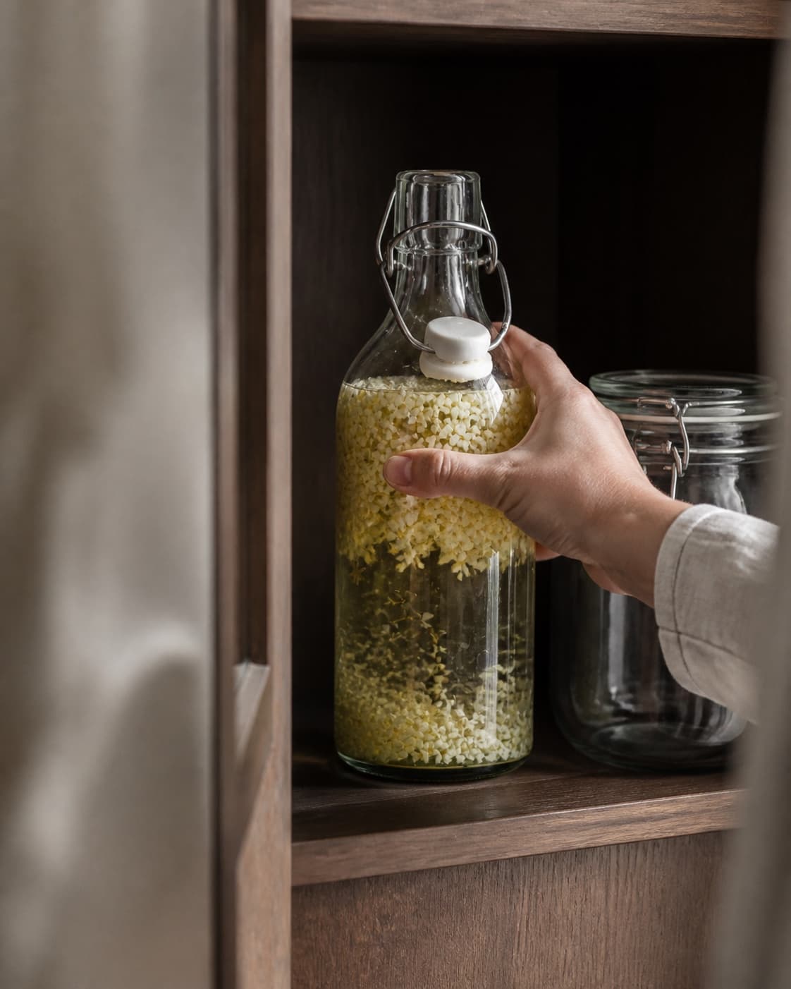 One single photorealistic instructional frame of the sealed infusion jar resting in a dark cupboard for Hyldeblomst vodka, featuring vodka, hyldeblomstskærme, økologisk citron, with only the named equipment and no unrelated food, text, logos or packaging under tilberedningen af hyldeblomst vodka