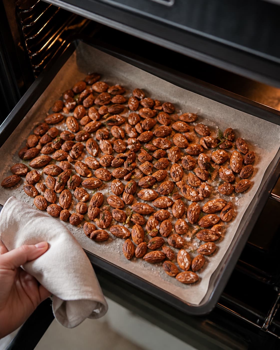 One single photorealistic instructional frame of the seasoned main ingredient roasting until properly cooked for Saltmandler med rosmarin, featuring mandler, groft salt, frisk rosmarin, with only the named equipment and no unrelated food, text, logos or packaging under tilberedningen af saltmandler med rosmarin
