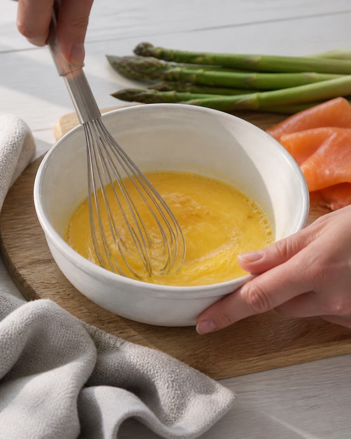 One single photorealistic instructional frame of eggs being whisked smoothly in one bowl for Æg bagt med laks og asparges, featuring æg, varmrøget laks, grønne asparges, with only the named equipment and no unrelated food, text, logos or packaging under tilberedningen af æg bagt med laks og asparges