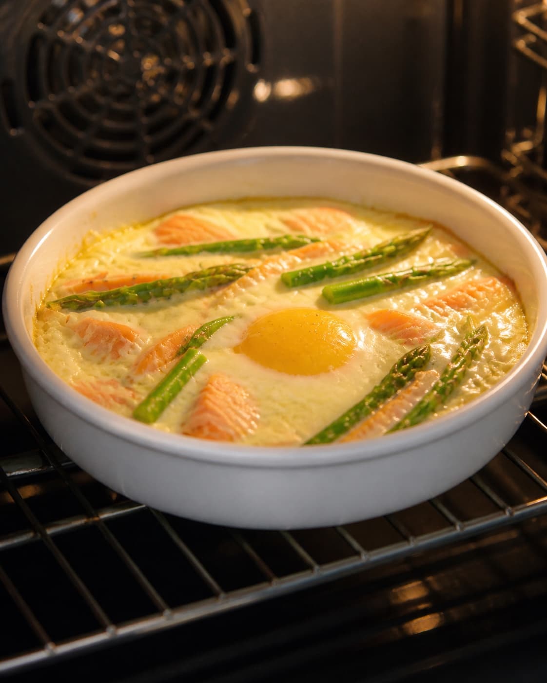 One single photorealistic instructional frame of the egg mixture gently setting around the filling for Æg bagt med laks og asparges, featuring æg, varmrøget laks, grønne asparges, with only the named equipment and no unrelated food, text, logos or packaging under tilberedningen af æg bagt med laks og asparges