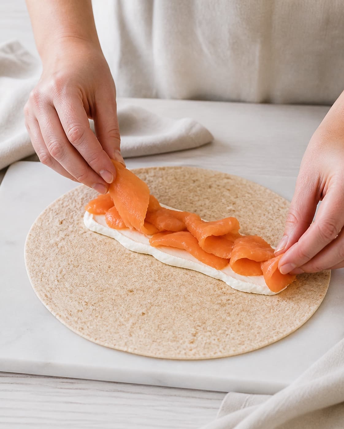One single photorealistic instructional frame of realistic hands arranging filling down the center of one wrap for Wraps med varmrøget laks, featuring tortillawraps, varmrøget laks, flødeost, with only the named equipment and no unrelated food, text, logos or packaging under tilberedningen af wraps med varmrøget laks
