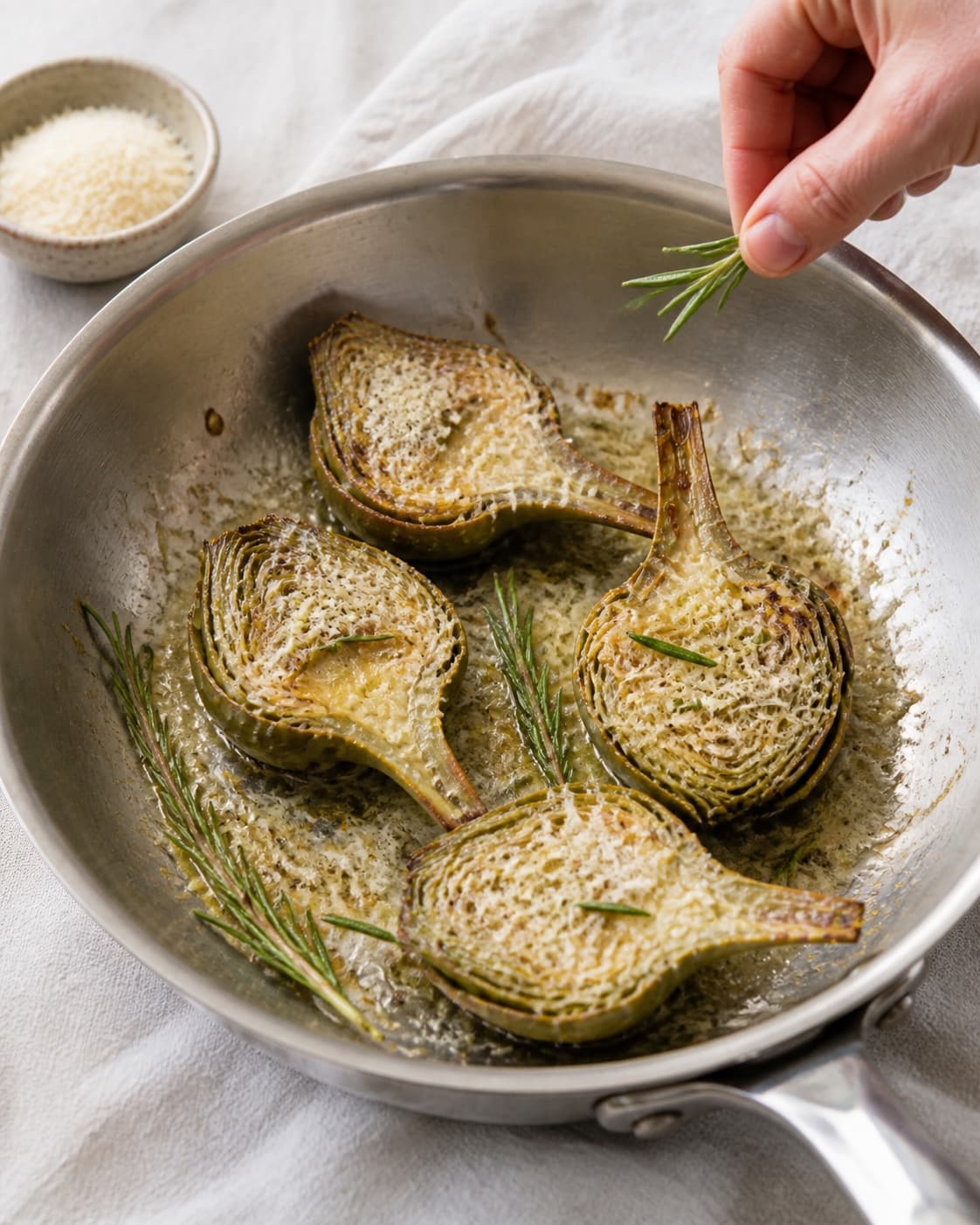 One single photorealistic instructional frame of the savoury filling browning in one skillet for Gratinerede artiskokker med parmesan og rosmarin, featuring artiskokhjerter, parmesan, frisk rosmarin, with only the named equipment and no unrelated food, text, logos or packaging under tilberedningen af gratinerede artiskokker med parmesan og rosmarin