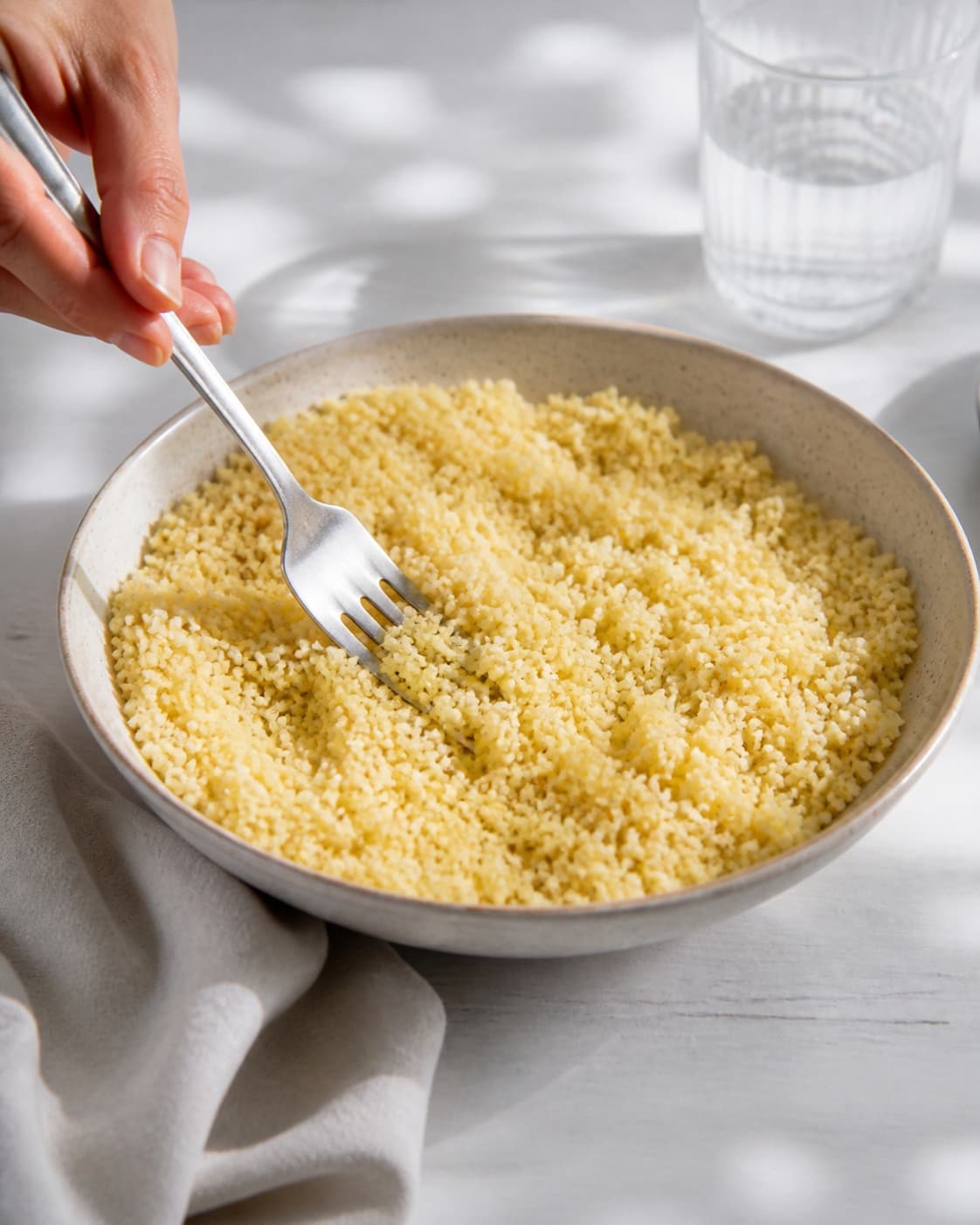 One bowl of fluffy hydrated couscous being loosened with a fork, no vegetables, dressing, roasting tray or finished salad under tilberedningen af couscous salat