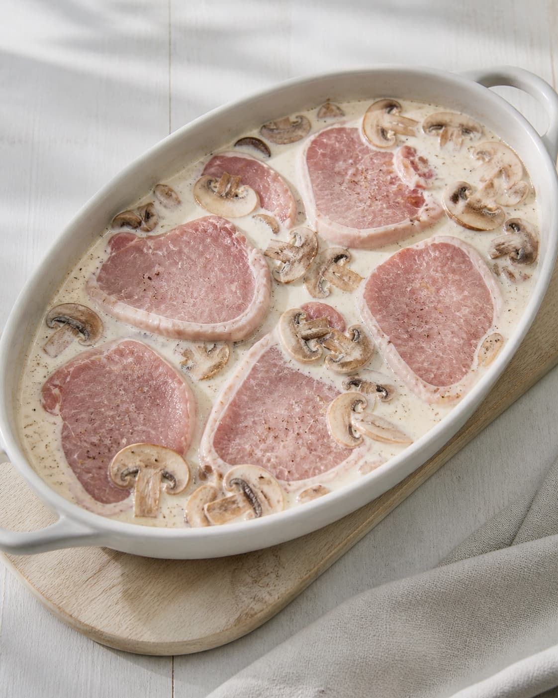 One single photorealistic instructional frame of the unbaked casserole assembled in one clean dish for Koteletter og champignon i fad, featuring svinekoteletter, champignon, piskefløde, with only the named equipment and no unrelated food, text, logos or packaging under tilberedningen af koteletter og champignon i fad