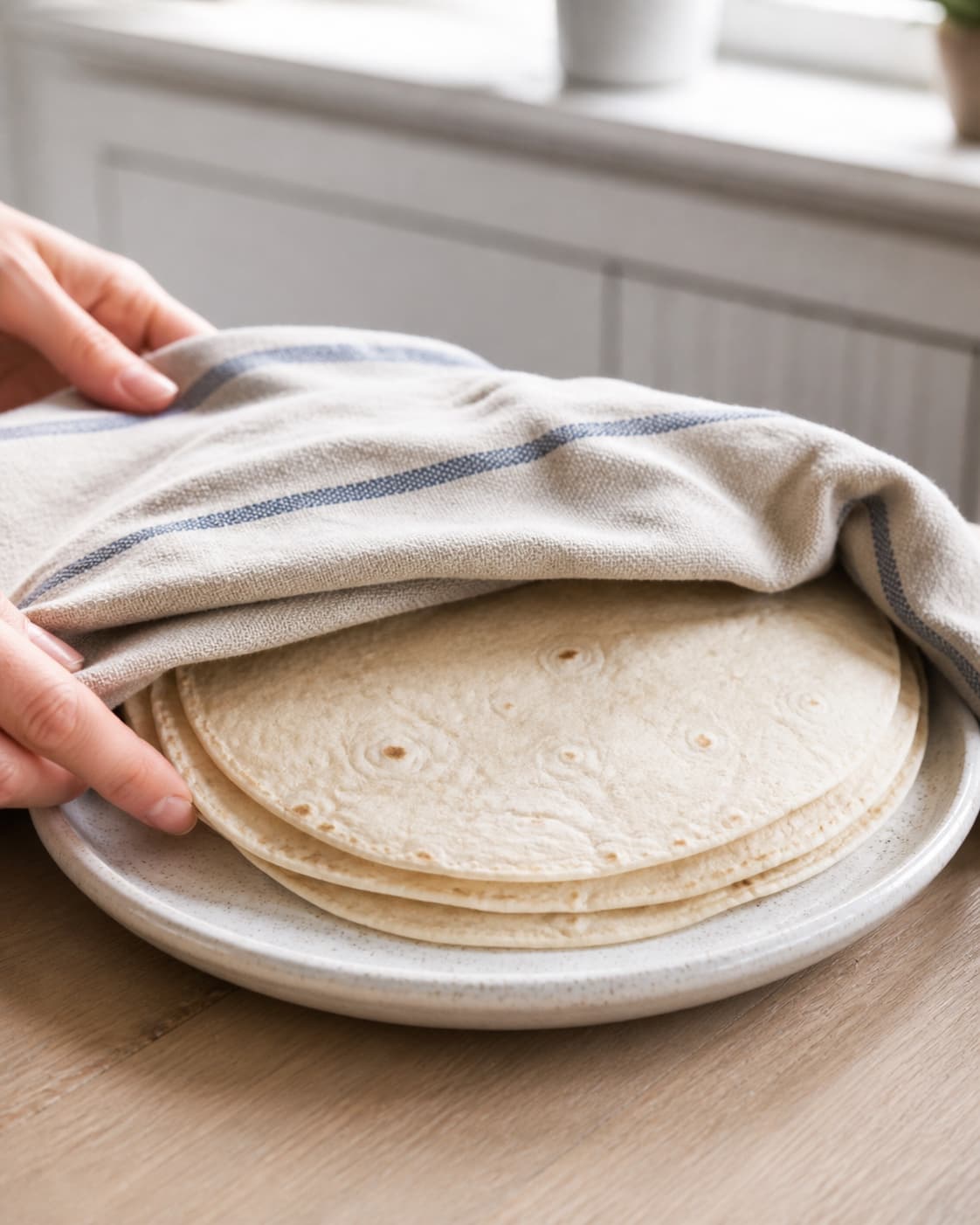 One single photorealistic instructional frame of soft flexible flatbreads warming under one cloth for Wraps med æggesalat, featuring tortillawraps, æg, mayonnaise, with only the named equipment and no unrelated food, text, logos or packaging under tilberedningen af wraps med æggesalat