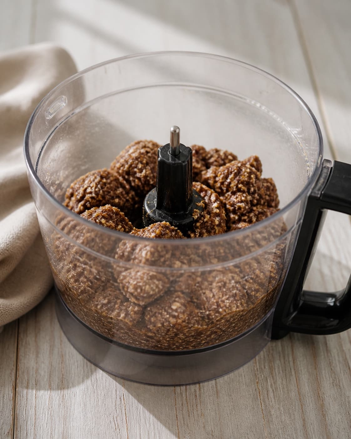 One single photorealistic instructional frame of the confection base becoming cohesive in one food processor for Energikugler, featuring dadler, havregryn, kakaopulver, with only the named equipment and no unrelated food, text, logos or packaging under tilberedningen af energikugler