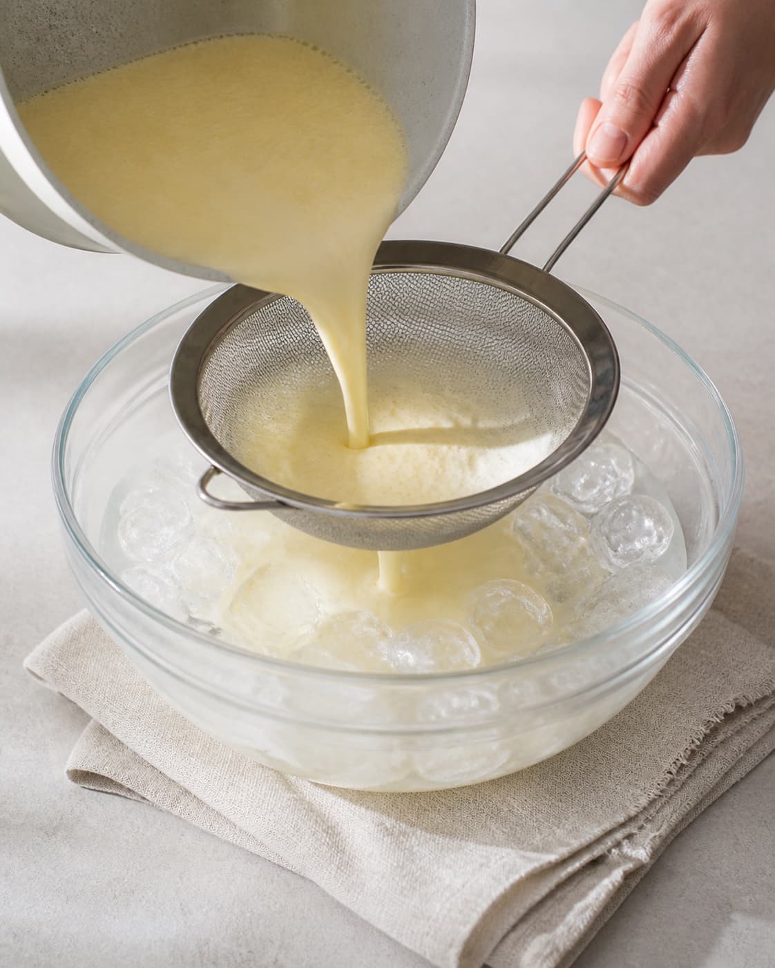 One single photorealistic instructional frame of the strained custard cooling in an ice bath for Lakrids Flødeis, featuring piskefløde, sødmælk, æggeblommer, with only the named equipment and no unrelated food, text, logos or packaging under tilberedningen af lakrids flødeis