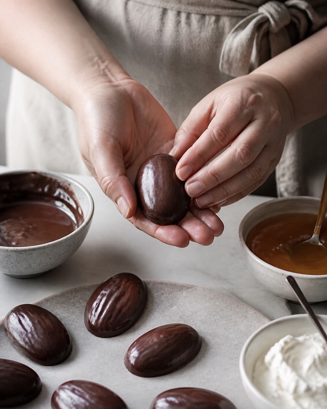 One single photorealistic instructional frame of realistic hands shaping equal confection pieces for Skildpadder med rom, featuring mørk chokolade, karamel, piskefløde, with only the named equipment and no unrelated food, text, logos or packaging under tilberedningen af skildpadder med rom
