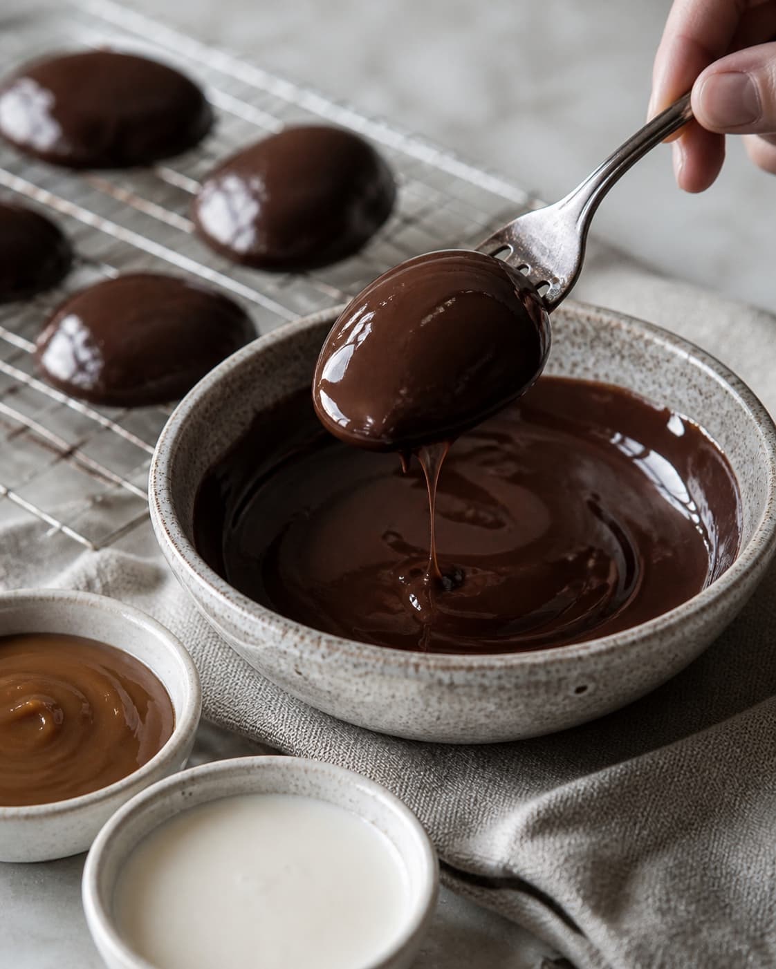 One single photorealistic instructional frame of the shaped pieces receiving an even coating for Skildpadder med rom, featuring mørk chokolade, karamel, piskefløde, with only the named equipment and no unrelated food, text, logos or packaging under tilberedningen af skildpadder med rom