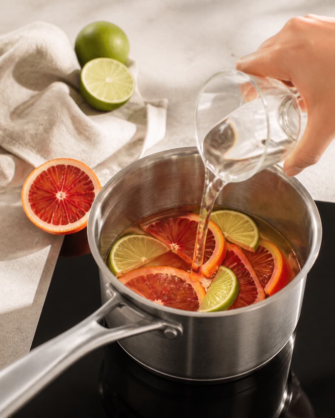 One single photorealistic instructional frame of the aromatic drink base being prepared in one small saucepan for Blodappelsin Mojito, featuring hvid rom, blodappelsiner, lime, with only the named equipment and no unrelated food, text, logos or packaging under tilberedningen af blodappelsin mojito