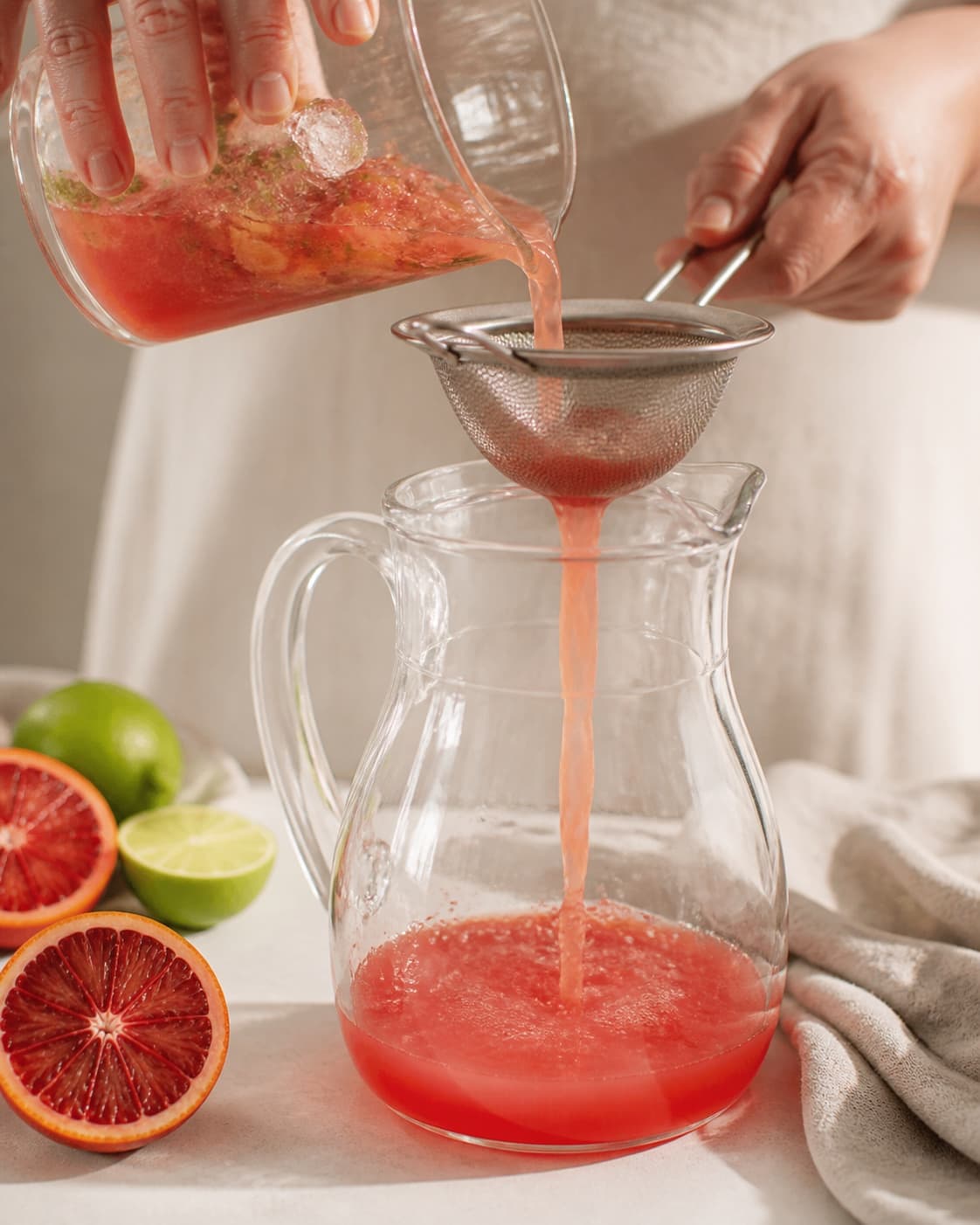 One single photorealistic instructional frame of a strained drink base cooling in one clear jug for Blodappelsin Mojito, featuring hvid rom, blodappelsiner, lime, with only the named equipment and no unrelated food, text, logos or packaging under tilberedningen af blodappelsin mojito
