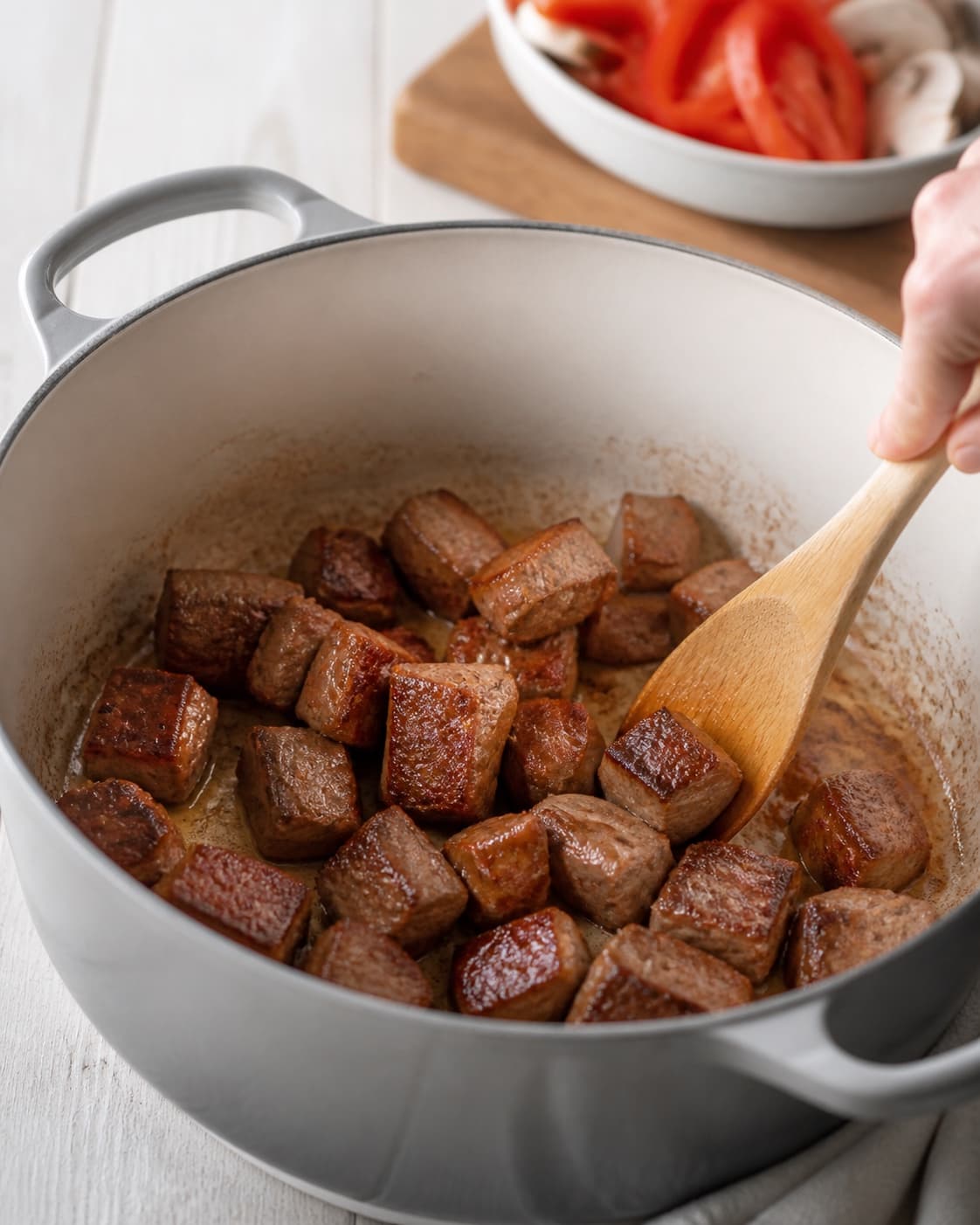 One single photorealistic instructional frame of meat cubes searing deeply brown in one heavy pot for Paprikagryde - en klassisk mørbradgryde, featuring svinemørbrad, rød peberfrugt, champignon, with only the named equipment and no unrelated food, text, logos or packaging under tilberedningen af paprikagryde - en klassisk mørbradgryde