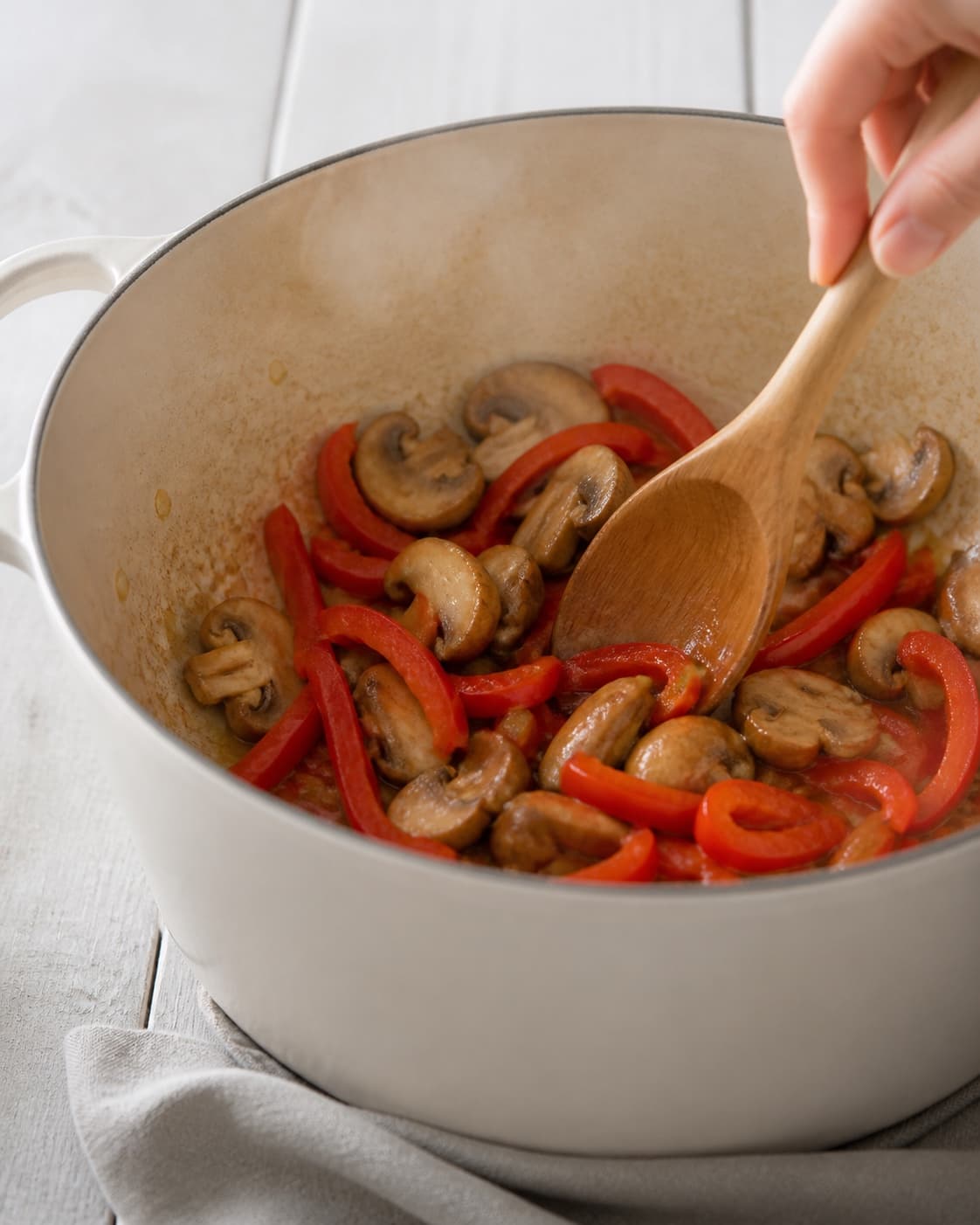 One single photorealistic instructional frame of aromatic vegetables softening in the same heavy pot for Paprikagryde - en klassisk mørbradgryde, featuring svinemørbrad, rød peberfrugt, champignon, with only the named equipment and no unrelated food, text, logos or packaging under tilberedningen af paprikagryde - en klassisk mørbradgryde