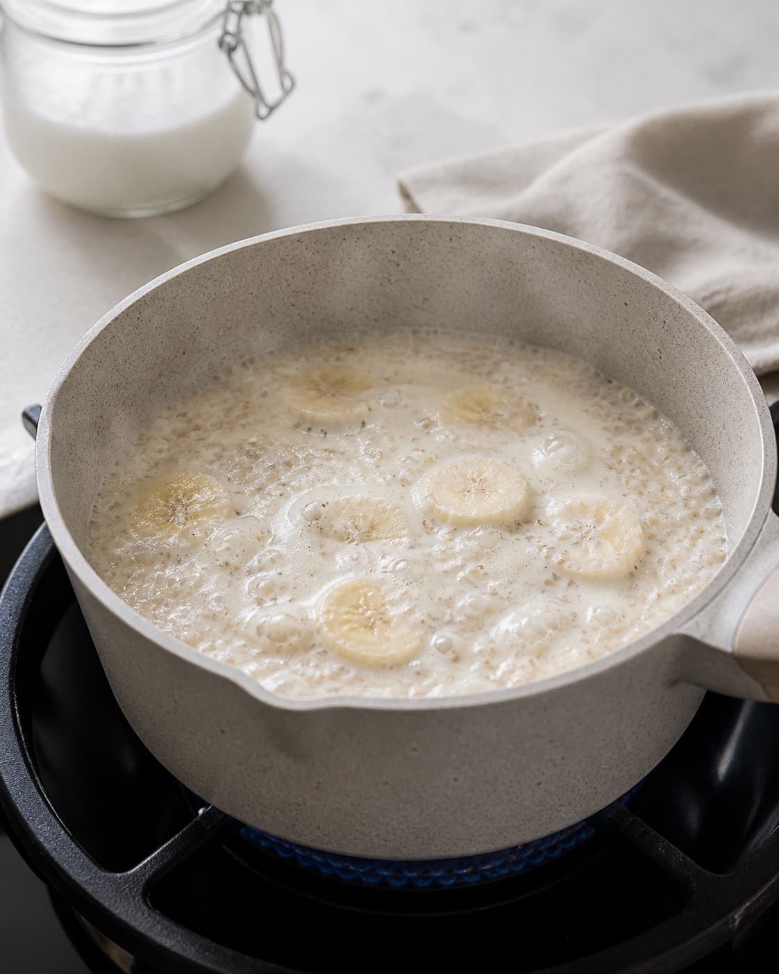 One single photorealistic instructional frame of creamy breakfast porridge gently simmering in one pot for Quinoagrød med kokos og banan, featuring quinoa, kokosmælk, bananer, with only the named equipment and no unrelated food, text, logos or packaging under tilberedningen af quinoagrød med kokos og banan