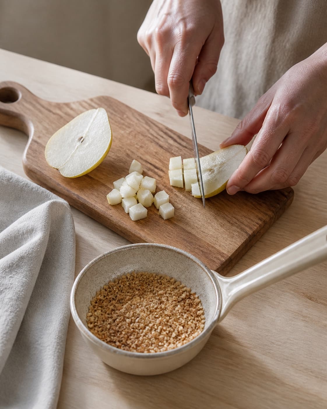 One single photorealistic instructional frame of fresh fruit being cut beside one small pan of toasted topping for Krydret morgengrød, featuring havregryn, mælk, pære, with only the named equipment and no unrelated food, text, logos or packaging under tilberedningen af krydret morgengrød