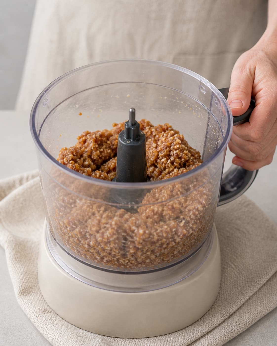 One single photorealistic instructional frame of the confection base becoming cohesive in one food processor for Abrikos og kokos konfektkugler, featuring tørrede abrikoser, kokosmel, dadler, with only the named equipment and no unrelated food, text, logos or packaging under tilberedningen af abrikos og kokos konfektkugler