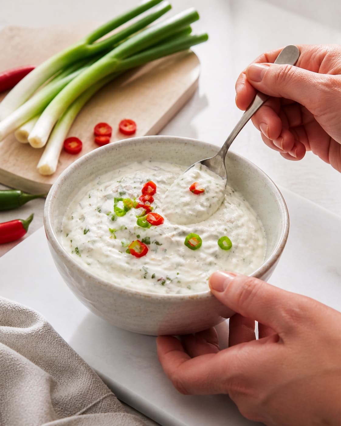 One single photorealistic instructional frame of one bowl of finished dip being tasted and adjusted for 3 x hjemmelavet dip til chips, featuring cremefraiche 18 %, forårsløg, rød chili, with only the named equipment and no unrelated food, text, logos or packaging under tilberedningen af 3 x hjemmelavet dip til chips