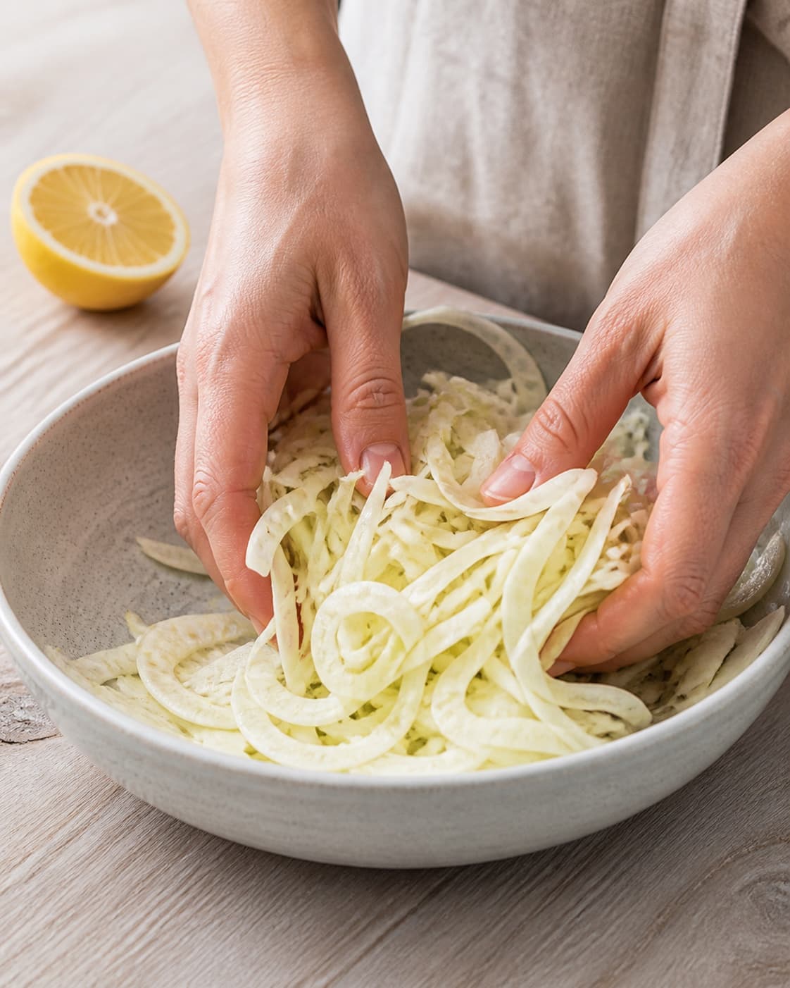 Thin raw fennel slices being gently massaged with lemon in one bowl, no oven, roasting tray, blueberries, pear or finished salad under tilberedningen af fennikelsalat med blåbær og pære