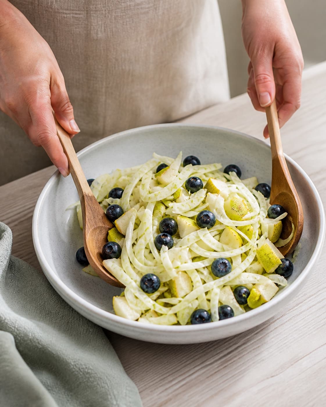 One single photorealistic instructional frame of the prepared salad components being gently tossed together for Fennikelsalat med blåbær og pære, featuring fennikel, blåbær, pærer, with only the named equipment and no unrelated food, text, logos or packaging under tilberedningen af fennikelsalat med blåbær og pære