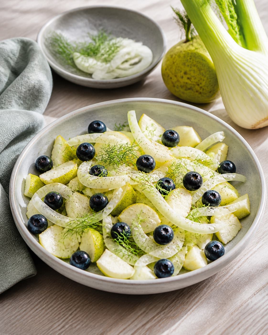 One single photorealistic instructional frame of the finished salad arranged loosely on one serving platter for Fennikelsalat med blåbær og pære, featuring fennikel, blåbær, pærer, with only the named equipment and no unrelated food, text, logos or packaging under tilberedningen af fennikelsalat med blåbær og pære