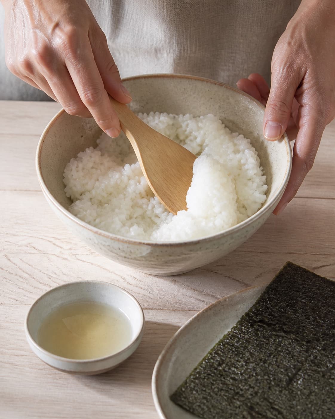 One single photorealistic instructional frame of sushi rice being gently folded with seasoning for Sushi i madpakken - lækre maki med laks, featuring sushiris, riseddike, noriark, with only the named equipment and no unrelated food, text, logos or packaging under tilberedningen af sushi i madpakken - lækre maki med laks