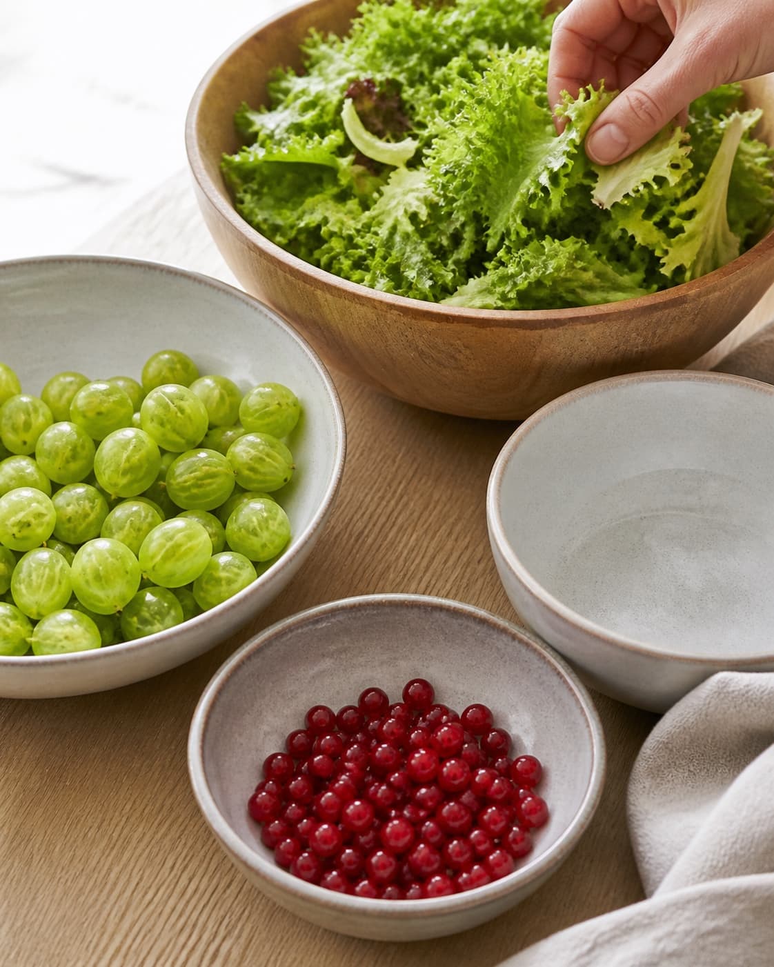 One single photorealistic instructional frame of washed and evenly cut raw ingredients arranged in separate bowls for Sommersalat med stikkelsbær og ribs, featuring blandede salatblade, stikkelsbær, ribs, with only the named equipment and no unrelated food, text, logos or packaging under tilberedningen af sommersalat med stikkelsbær og ribs