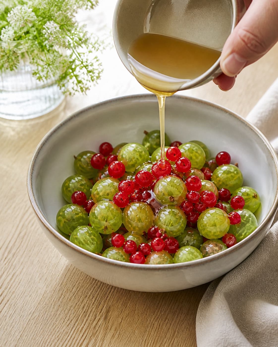 Fresh whole gooseberries and red currants being gently macerated with honey in one bowl, no oven, roasting tray, lettuce or finished salad under tilberedningen af sommersalat med stikkelsbær og ribs