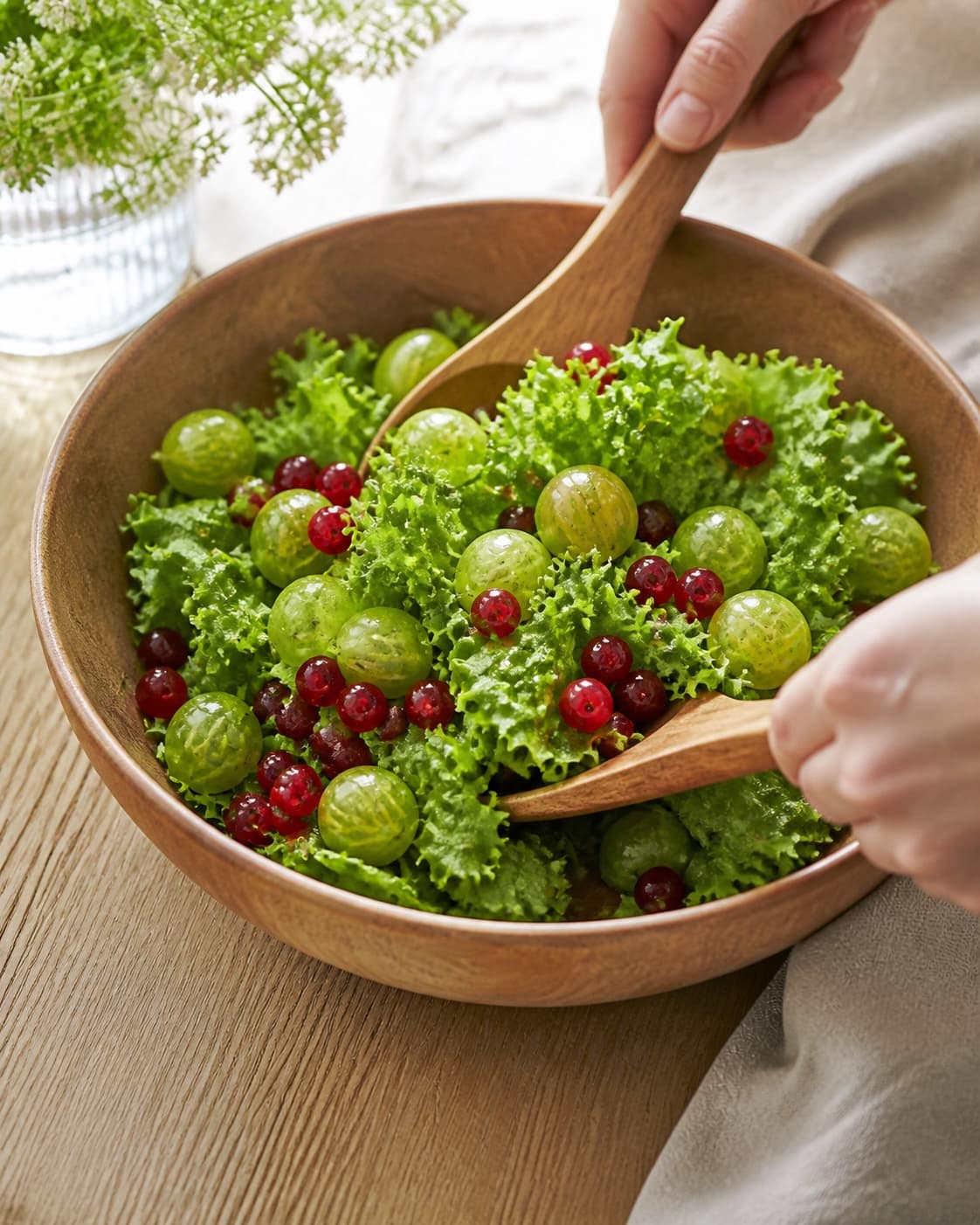 One single photorealistic instructional frame of the prepared salad components being gently tossed together for Sommersalat med stikkelsbær og ribs, featuring blandede salatblade, stikkelsbær, ribs, with only the named equipment and no unrelated food, text, logos or packaging under tilberedningen af sommersalat med stikkelsbær og ribs