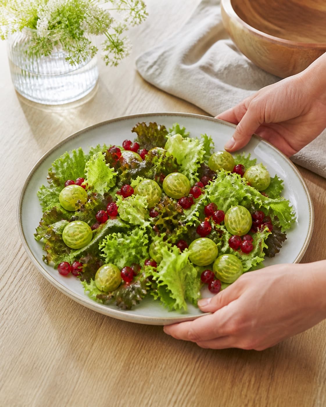 One single photorealistic instructional frame of the finished salad arranged loosely on one serving platter for Sommersalat med stikkelsbær og ribs, featuring blandede salatblade, stikkelsbær, ribs, with only the named equipment and no unrelated food, text, logos or packaging under tilberedningen af sommersalat med stikkelsbær og ribs