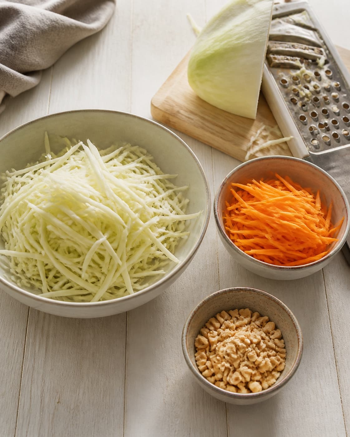 One single photorealistic instructional frame of washed and evenly cut raw ingredients arranged in separate bowls for Papayasalat - vietnamesisk, featuring grøn papaya, gulerødder, peanuts, with only the named equipment and no unrelated food, text, logos or packaging under tilberedningen af papayasalat - vietnamesisk