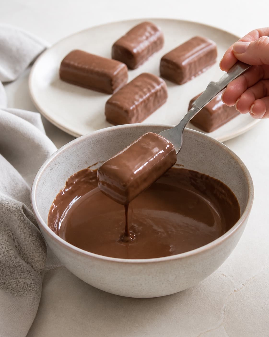 One single photorealistic instructional frame of the shaped pieces receiving an even coating for Hjemmelavet twix, featuring hvedemel, smør, sukker, with only the named equipment and no unrelated food, text, logos or packaging under tilberedningen af hjemmelavet twix
