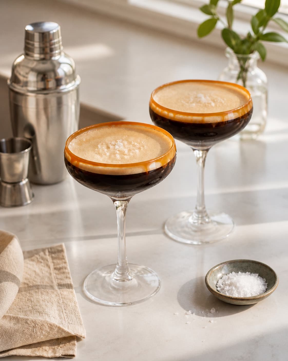 One single photorealistic instructional frame of the completed drink in clean chilled glasses with restrained garnish for Espresso Martini med saltkaramel, featuring vodka, espresso, kaffelikør, with only the named equipment and no unrelated food, text, logos or packaging under tilberedningen af espresso martini med saltkaramel
