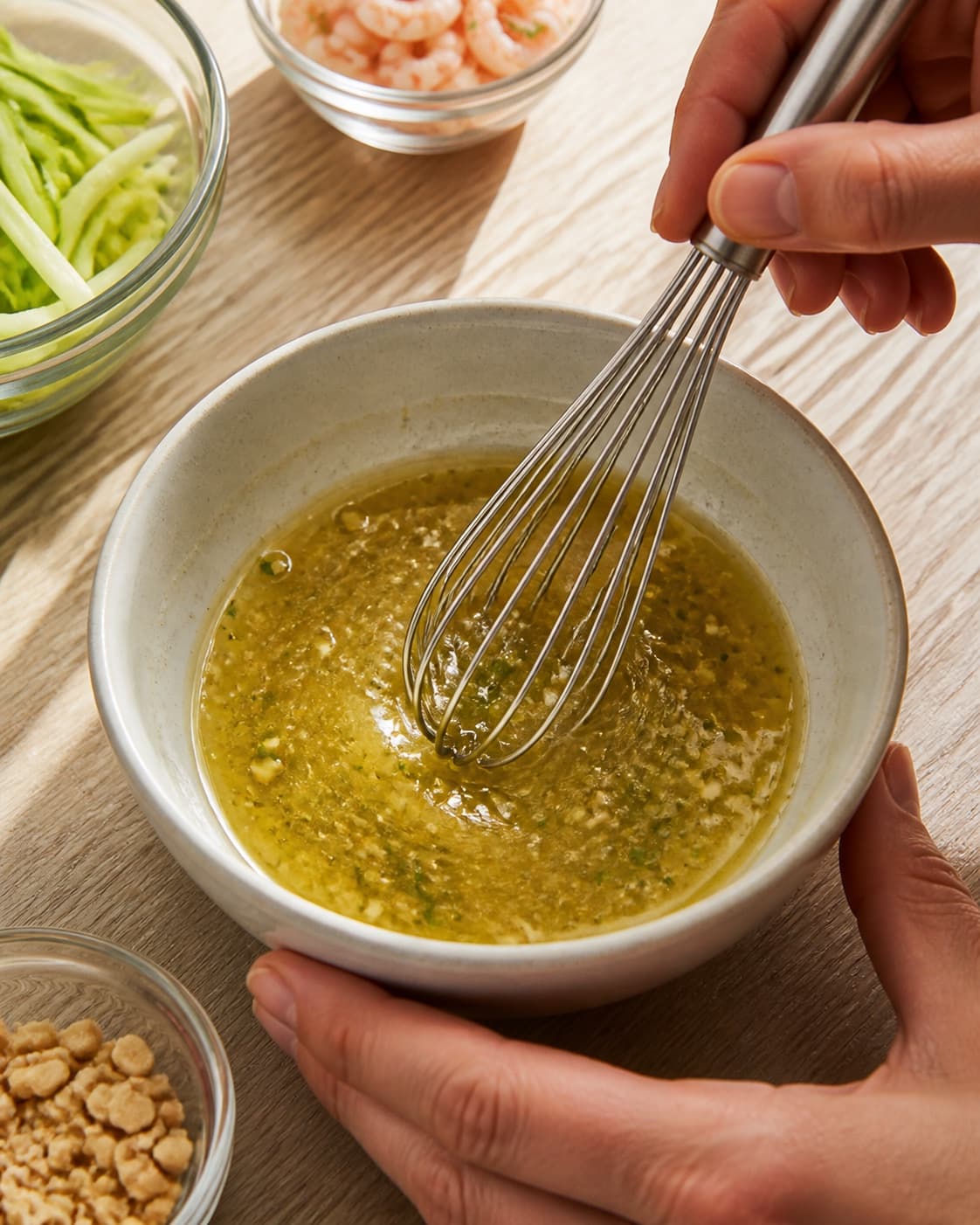 One single photorealistic instructional frame of a glossy dressing being whisked in one small bowl for Grøn mango salat med rejer, featuring grøn mango, rejer, peanuts, with only the named equipment and no unrelated food, text, logos or packaging under tilberedningen af grøn mango salat med rejer