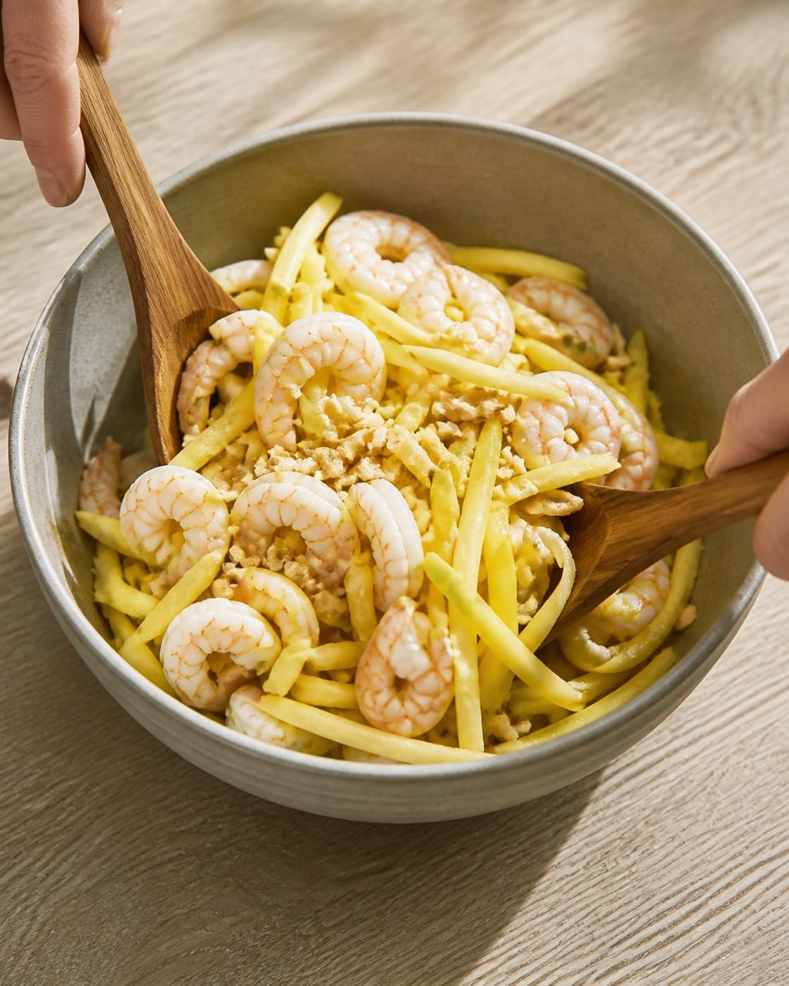 One single photorealistic instructional frame of the prepared salad components being gently tossed together for Grøn mango salat med rejer, featuring grøn mango, rejer, peanuts, with only the named equipment and no unrelated food, text, logos or packaging under tilberedningen af grøn mango salat med rejer