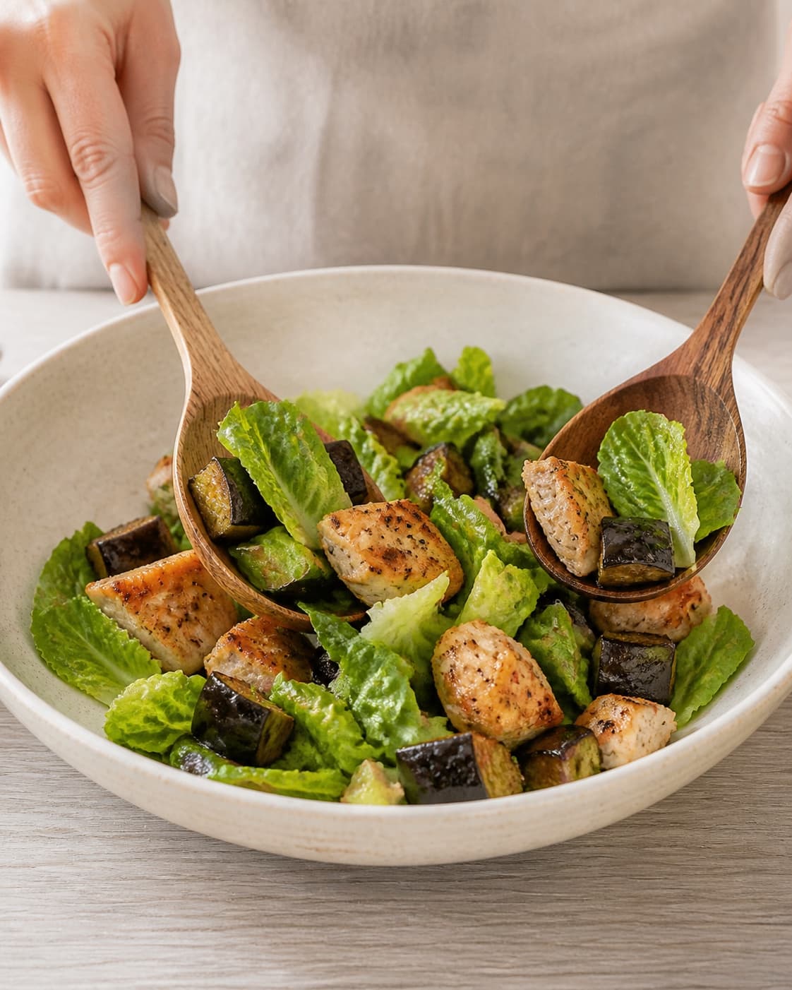 One single photorealistic instructional frame of the prepared salad components being gently tossed together for Salat med Kylling og aubergine, featuring kyllingebryst, aubergine, romainesalat, with only the named equipment and no unrelated food, text, logos or packaging under tilberedningen af salat med kylling og aubergine