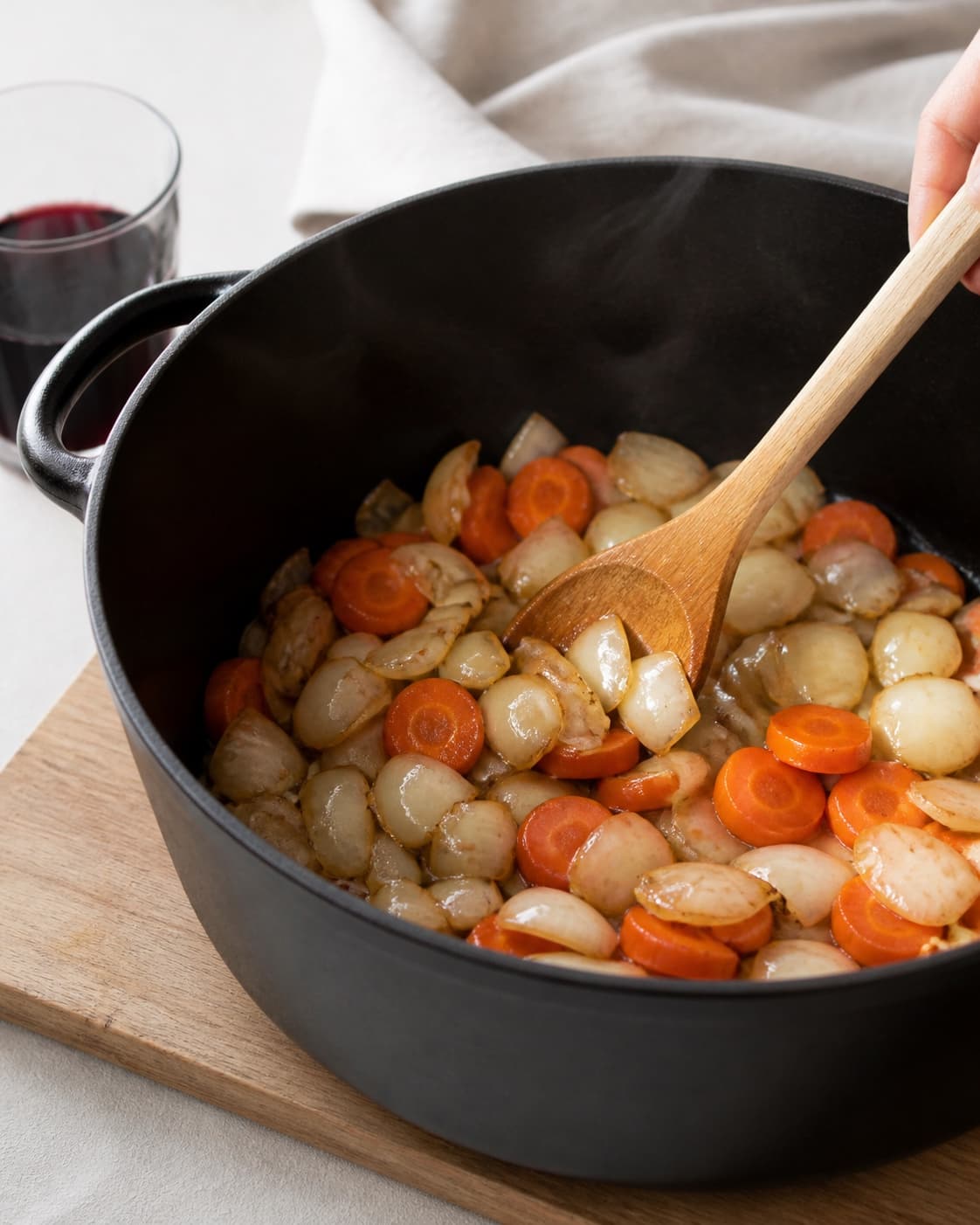 One single photorealistic instructional frame of aromatic vegetables softening in the same heavy pot for Boeuf Bourguignon, featuring oksebov, rødvin, gulerødder, with only the named equipment and no unrelated food, text, logos or packaging under tilberedningen af boeuf bourguignon