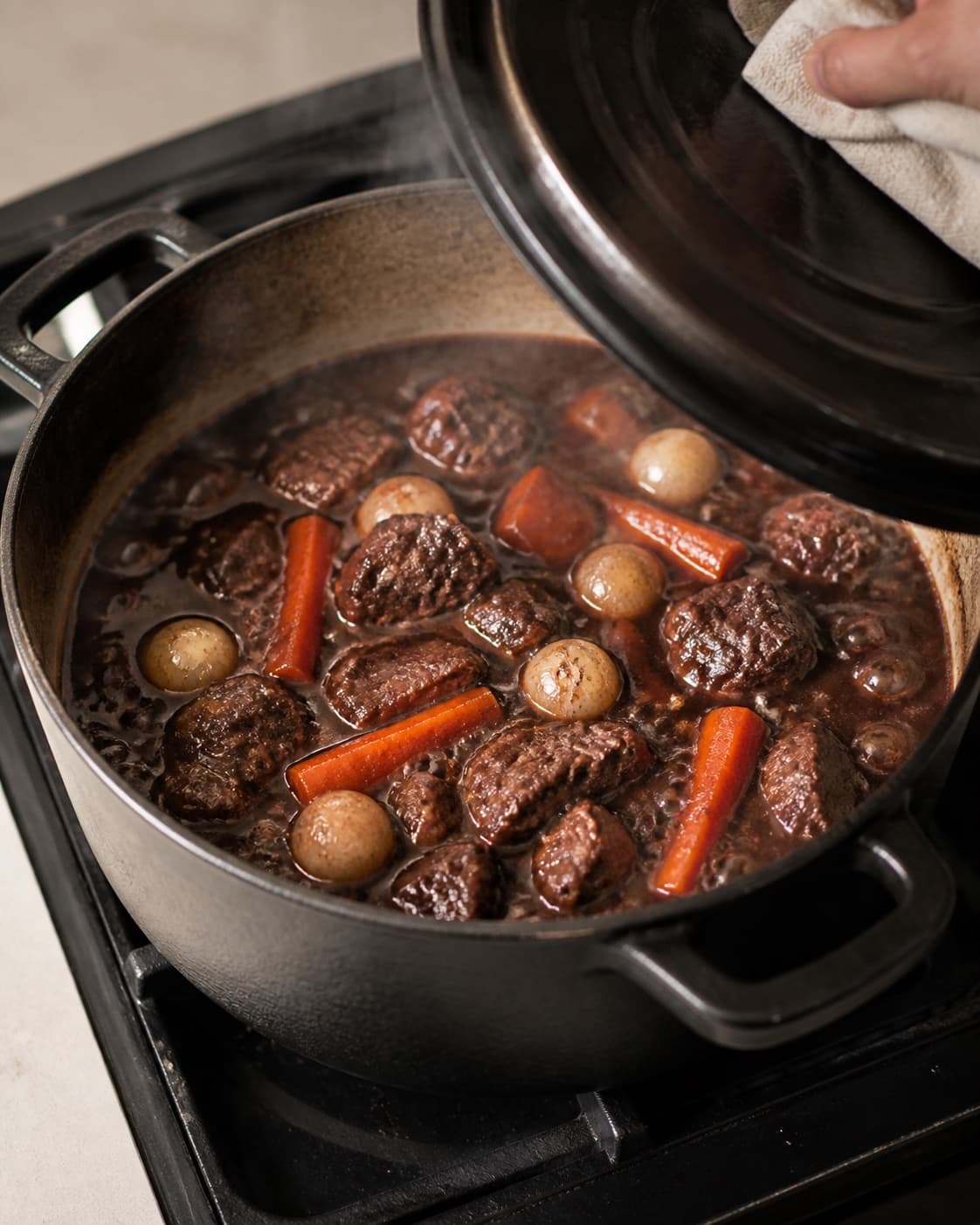 One single photorealistic instructional frame of the stew gently braising with tender meat and vegetables for Boeuf Bourguignon, featuring oksebov, rødvin, gulerødder, with only the named equipment and no unrelated food, text, logos or packaging under tilberedningen af boeuf bourguignon