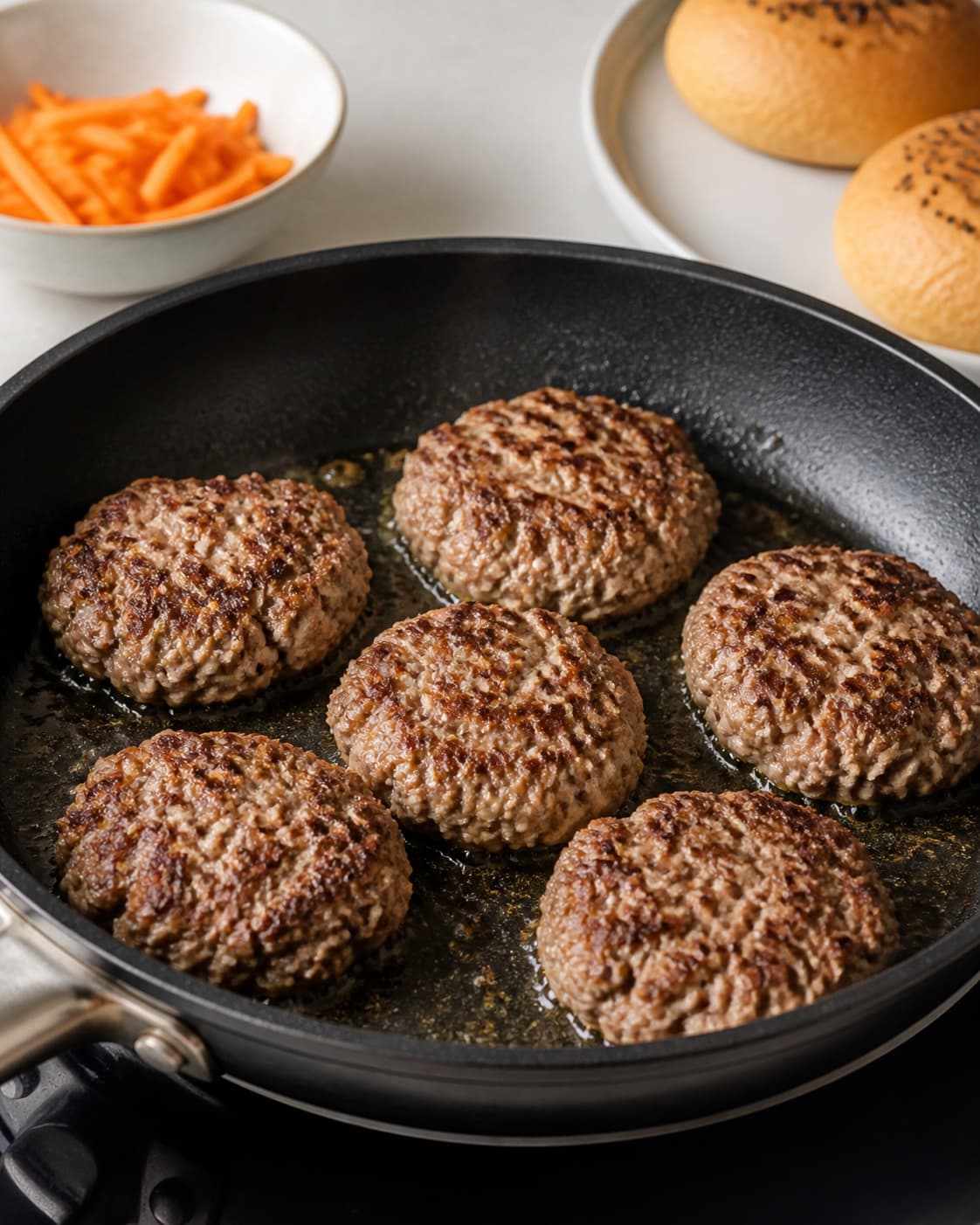 One single photorealistic instructional frame of burger patties browning in one skillet or grill for Banh Mi Burger, featuring hakket svinekød, burgerboller, gulerødder, with only the named equipment and no unrelated food, text, logos or packaging under tilberedningen af banh mi burger