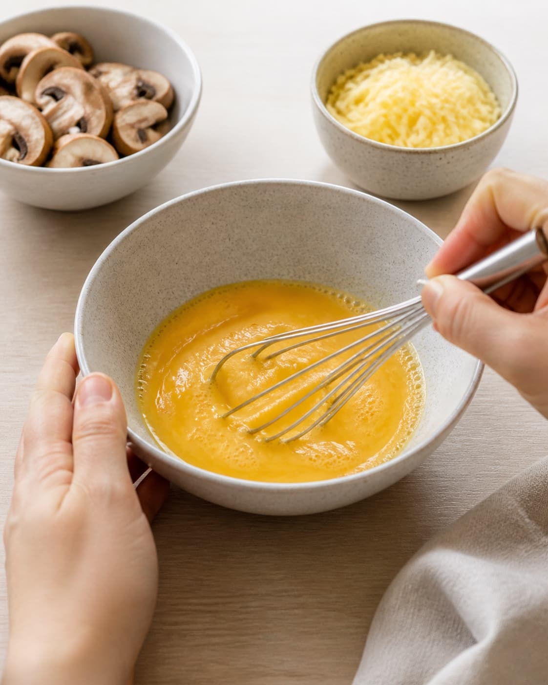 One single photorealistic instructional frame of eggs being whisked smoothly in one bowl for Omelet med svampe og ost, featuring æg, champignon, revet ost, with only the named equipment and no unrelated food, text, logos or packaging under tilberedningen af omelet med svampe og ost