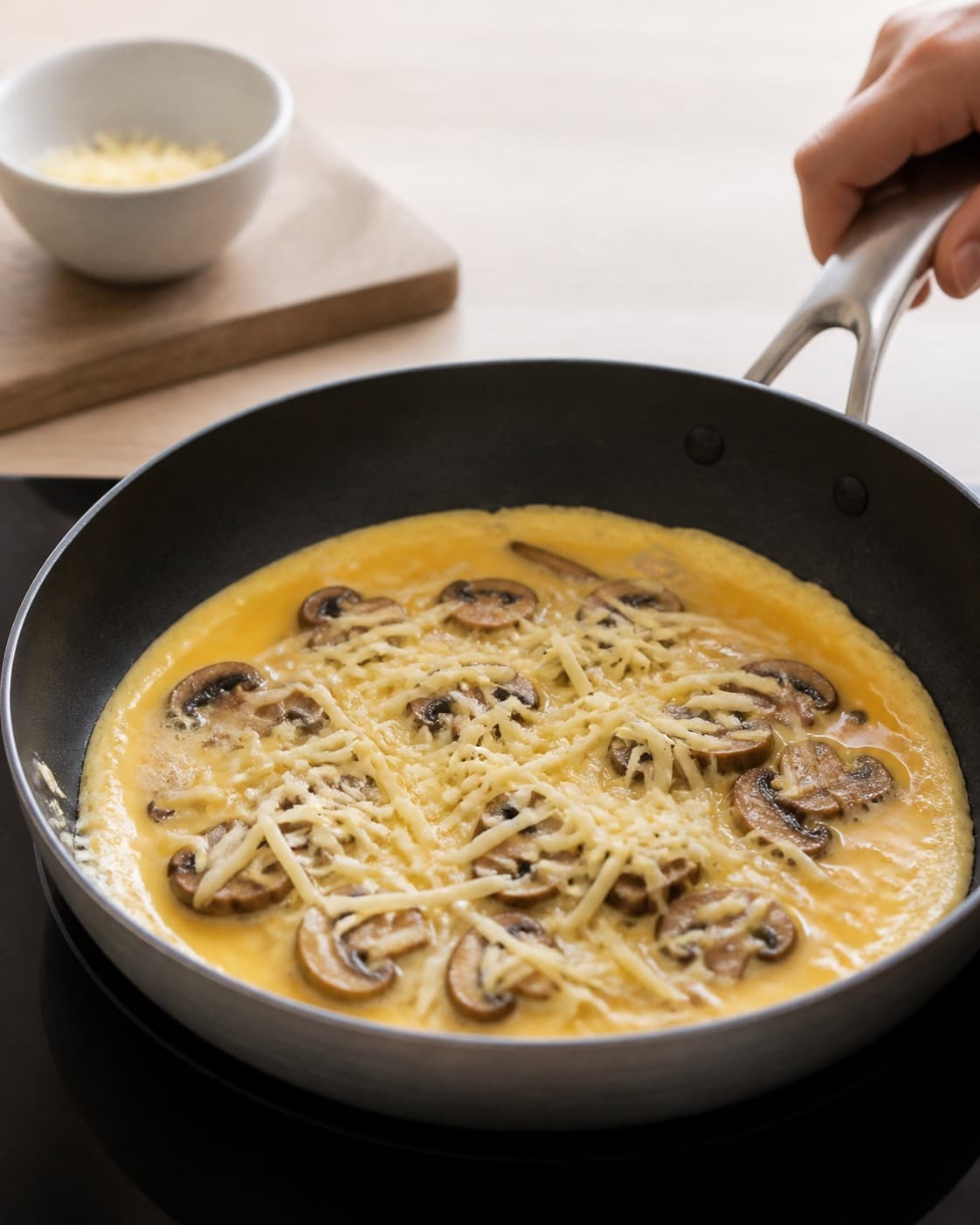 One single photorealistic instructional frame of the egg mixture gently setting around the filling for Omelet med svampe og ost, featuring æg, champignon, revet ost, with only the named equipment and no unrelated food, text, logos or packaging under tilberedningen af omelet med svampe og ost