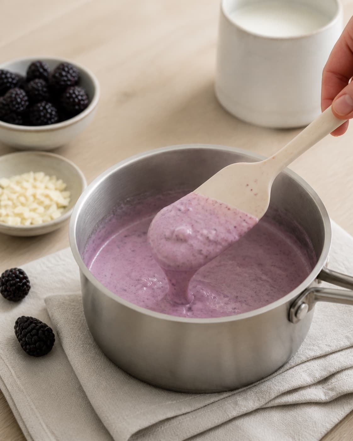 One single photorealistic instructional frame of the custard thickening gently on a spatula for Brombæris med hvid chokolade, featuring brombær, hvid chokolade, piskefløde, with only the named equipment and no unrelated food, text, logos or packaging under tilberedningen af brombæris med hvid chokolade