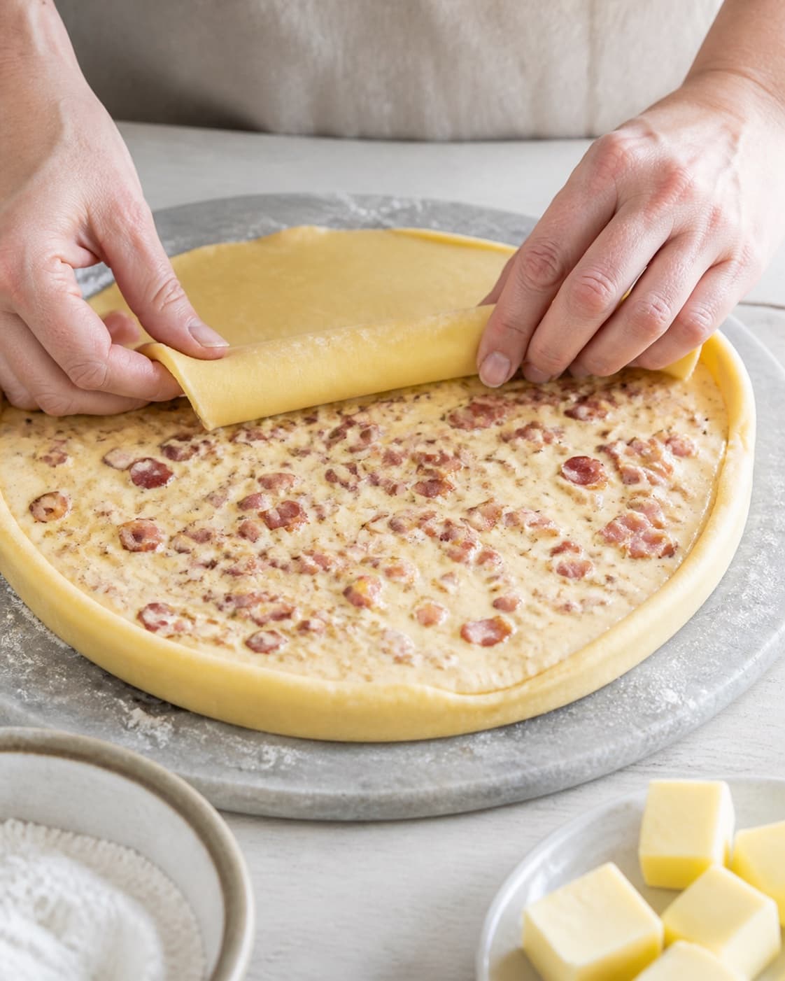 One single photorealistic instructional frame of pastry being rolled filled and sealed by realistic hands for Quiche lorraine, featuring hvedemel, smør, bacon, with only the named equipment and no unrelated food, text, logos or packaging under tilberedningen af quiche lorraine