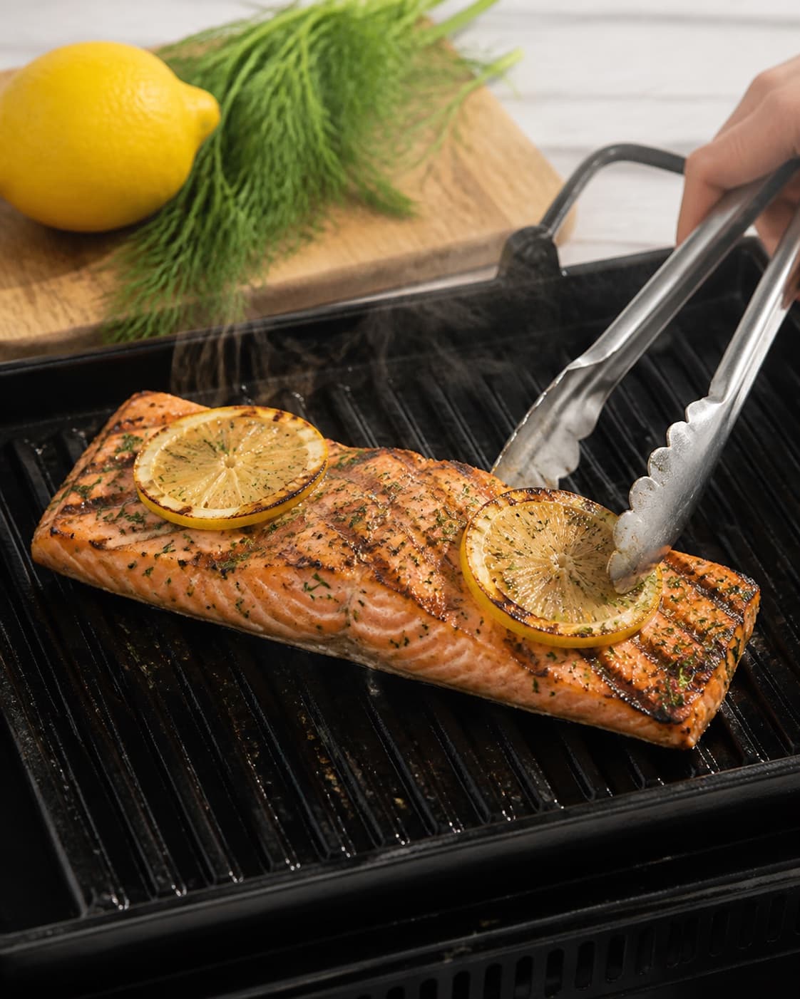 One single photorealistic instructional frame of the main ingredient grilling with clear sear marks for Laks på grill med citron og krydderurter, featuring lakseside, citron, frisk dild, with only the named equipment and no unrelated food, text, logos or packaging under tilberedningen af laks på grill med citron og krydderurter