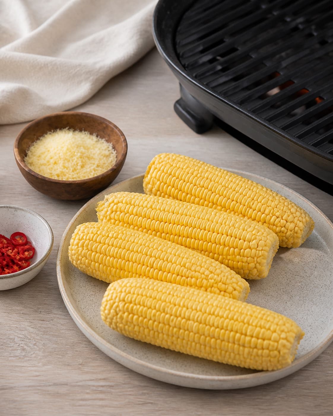 One single photorealistic instructional frame of the cleaned main ingredient prepared beside the grill for Majskolber med parmesan og chili, featuring majskolber, parmesan, chili, with only the named equipment and no unrelated food, text, logos or packaging under tilberedningen af majskolber med parmesan og chili